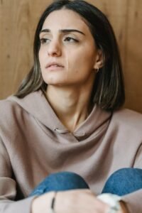 A young woman sitting indoors, appearing emotional with a tear on her cheek, depicting sadness.